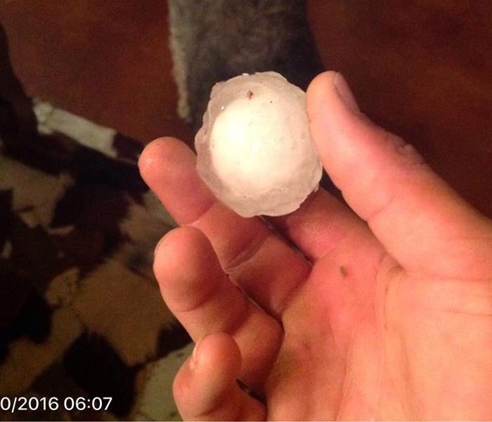 A hand holding a piece of hail the size of a golf ball