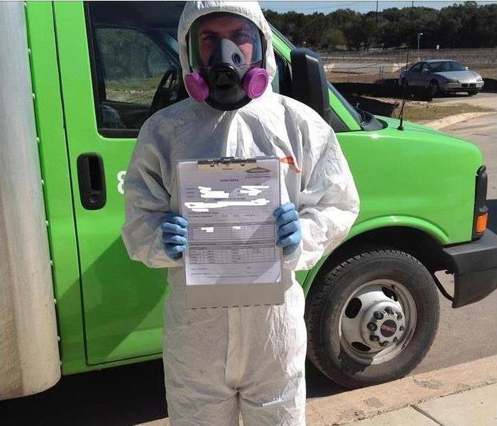 SERVPRO employee in a hazmat suit holding up a mold certificate