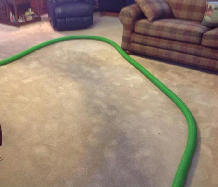 Dirty carpet in living room with SERVPRO green hose